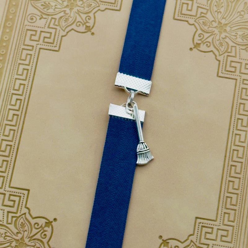 A silver broom charm on an elastic Bookband